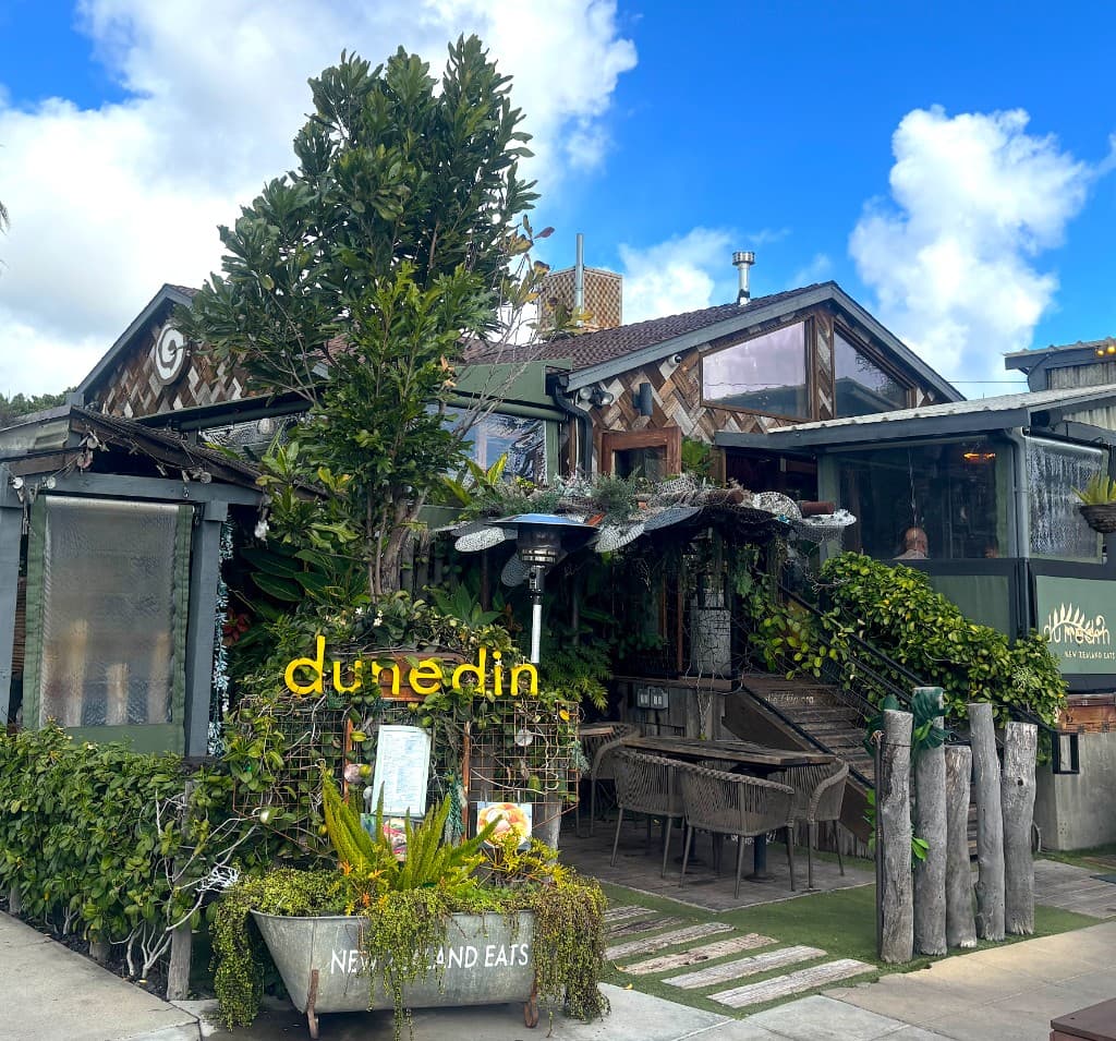 Dunedin restaurant exterior with neon sign, greenery and outdoor seating